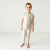 A young boy in a Makemake Organics Organic Tee & Pants Set - Cactus stands barefoot, smiling, in a plain white studio setting.