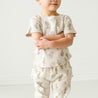 A toddler stands with arms crossed, wearing a short-sleeved shirt and Makemake Organics Organic Harem Pants - Cactus set, against a plain white background.