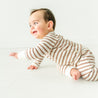 A joyful toddler in a Makemake Organics Organic Kimono Top & Pants Set - Stripes crawls on a white floor, smiling and reaching forward with one arm.