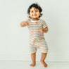 Toddler boy with curly hair, smiling and pointing, wearing a Makemake Organics Organic Short Zip Romper - Stripes against a plain white background.
