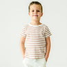 A young boy in a Makemake Organics Organic Tee & Pants Set - Stripes standing with hands in pockets, smiling against a plain background.