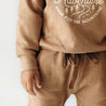 Close-up of a person wearing a cozy brown sweatshirt and Organic Jogger Pants in Cocoa from Organic Baby with the phrase "adventure made for the mountains" printed on the shirt. Only the torso and