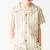 A toddler wearing a Makemake Organics Organic Linen Shirt and Shorts Set in Beige Stripes stands against a white background, with the focus on the shirt and the lower part of the face, excluding the eyes.