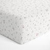 A close-up view of a crib fitted sheet with pillowcase from Makemake Organics that features a pattern of small, brown animal paw prints on a white background.