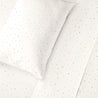 A white pillow and Makemake Organics Organic Cotton Sheet Set - Dotty with a pattern of small, colorful dots scattered across the surface, arranged in a clean and bright setting.