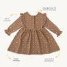 A flat lay of a long-sleeved, brown toddler dress from Organic Girls with white star patterns, highlighted features labeled: "gots certified," "snap buttons for gentle dressing.