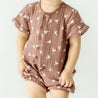 Toddler in a brown Makemake Organics Organic Muslin Short Bubble Romper with white bird pattern standing against a plain light background, face not visible.