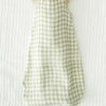 A light green and white Makemake Organics Muslin Wearable Blanket - Gingham laid out on a textured white surface.