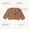 A flat-laid brown toddler's hoodie from Organic Baby labeled with features: "generously sized," "oversized hood," "gots certified cotton," "made with 100%