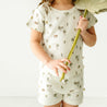 A child in the Organic Tee and Shorties Set - Malibu by Makemake Organics holds an upside-down large green leaf, covering part of their face, against a plain light background.