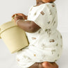 A toddler boy in a patterned onesie sits holding a pale yellow bucket, with a focus on the bucket and the child's back. The background is a soft, plain white.

Revised:
A toddler boy in an Organic Short Zip Romper - Malibu by Makemake Organics sits holding a pale yellow bucket, with a focus on the bucket and the child's back. The background is a soft, plain white.