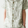 Close-up of a girl wearing an Organic Linen Shirt and Shorts Set - Palms by Makemake Organics, featuring three wooden buttons on the front. The focus is on the set's pattern and texture.