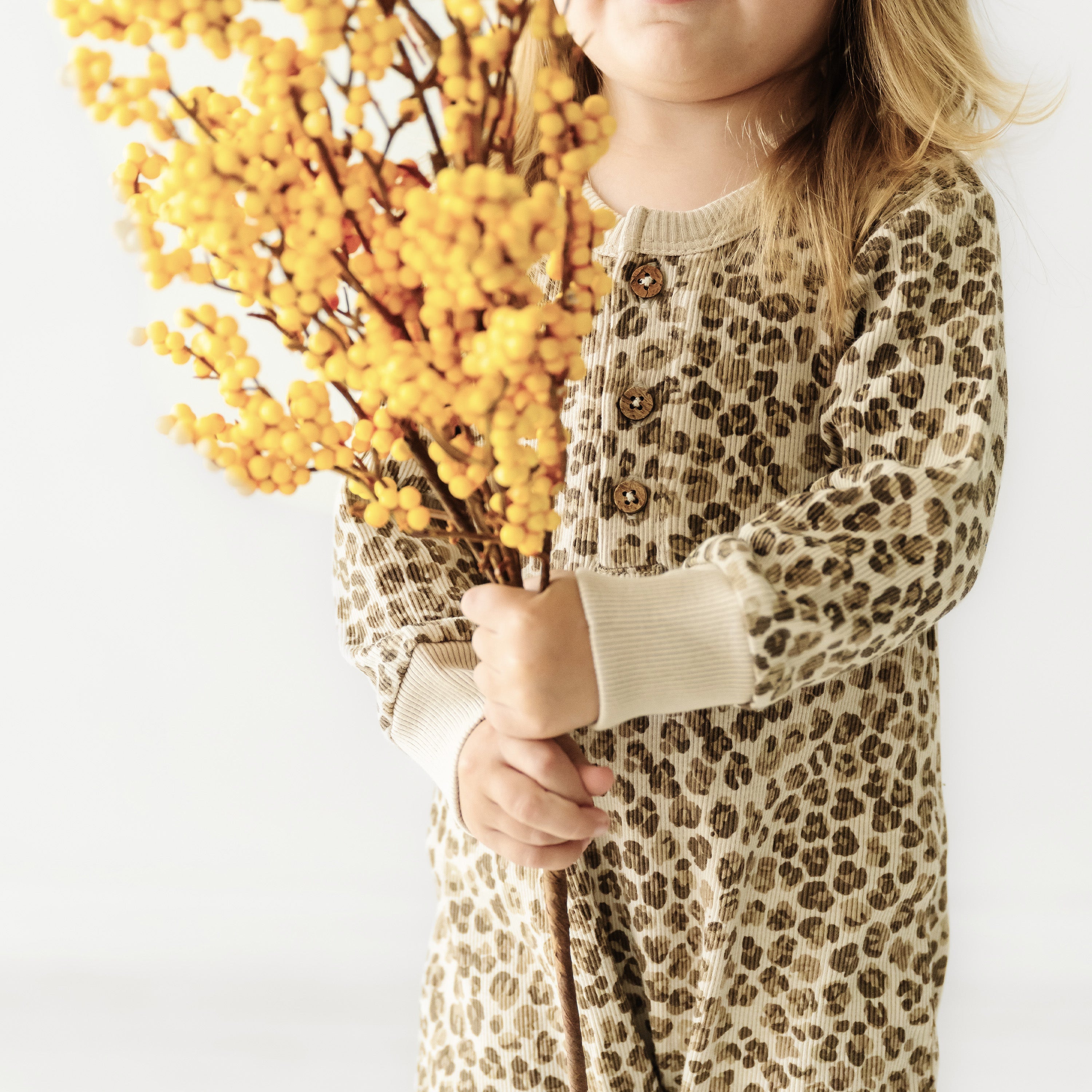 A young child, partially visible, holding a large bunch of yellow berries. the focus is on the vibrant berries, contrasting against the child's Organic Buttoned Romper - Spotted from Organic Baby.