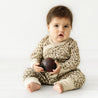 A baby wearing an Organic Baby Organic Kimono Onesie & Pants Set - Spotted outfit sits on a white floor holding a large red apple, looking inquisitively at the camera.