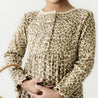 A close-up of a person wearing a long-sleeved, leopard print Organic Baby dress with button details, holding a straw hat partially, focusing on the dress and hands.