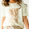 A toddler in a Boxy Tee and Skort Set - Summer Floral from Makemake Organics stands close-up, with the focus on the shirt and lowercase lettering.