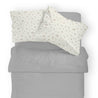 Top view of an unmade bed with a grey duvet and two pillows with a floral pattern on a light background featuring the Organic Cotton Toddler Pillowcase - Bloom by Makemake Organics.