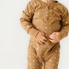 A baby in an Organic Baby brown Organic Buttoned Romper - Sparkle stands with its hands touching, against a plain white background, adorned with small white stars.