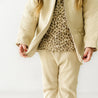A person in a trendy outfit from Organic Kids, featuring beige pants and a quilted jacket over a leopard print top, stands against a white background. Only the torso and arms are visible