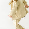 A young child in a matching organic merino wool zip jacket and pants set from Organic Kids dashes across a bright white background, with a focus on movement and playful energy, her hair flying behind her.