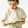 A young child in a Makemake Organics Organic Tee and Shorts Set - Pixie Dots shirt intently reading a book, isolated on a white background.