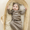 A baby in an Organic Baby speckle Kimono Knotted Sleep Gown lies in a wicker bassinet, looking up with a curious expression.